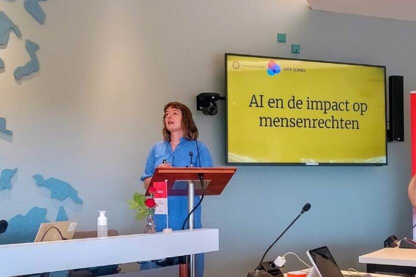 Iris Muis voor zaal achter katheder naast haar presentatie 'AI en inde impact op mensenrechten'